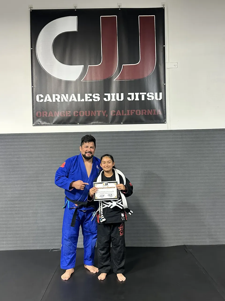 El profesor Rudy de Carnales Jiu Jitsu con una alumna que sostiene su certificado de promoción