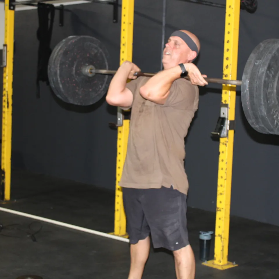 A member catching a barbell at his shoulders